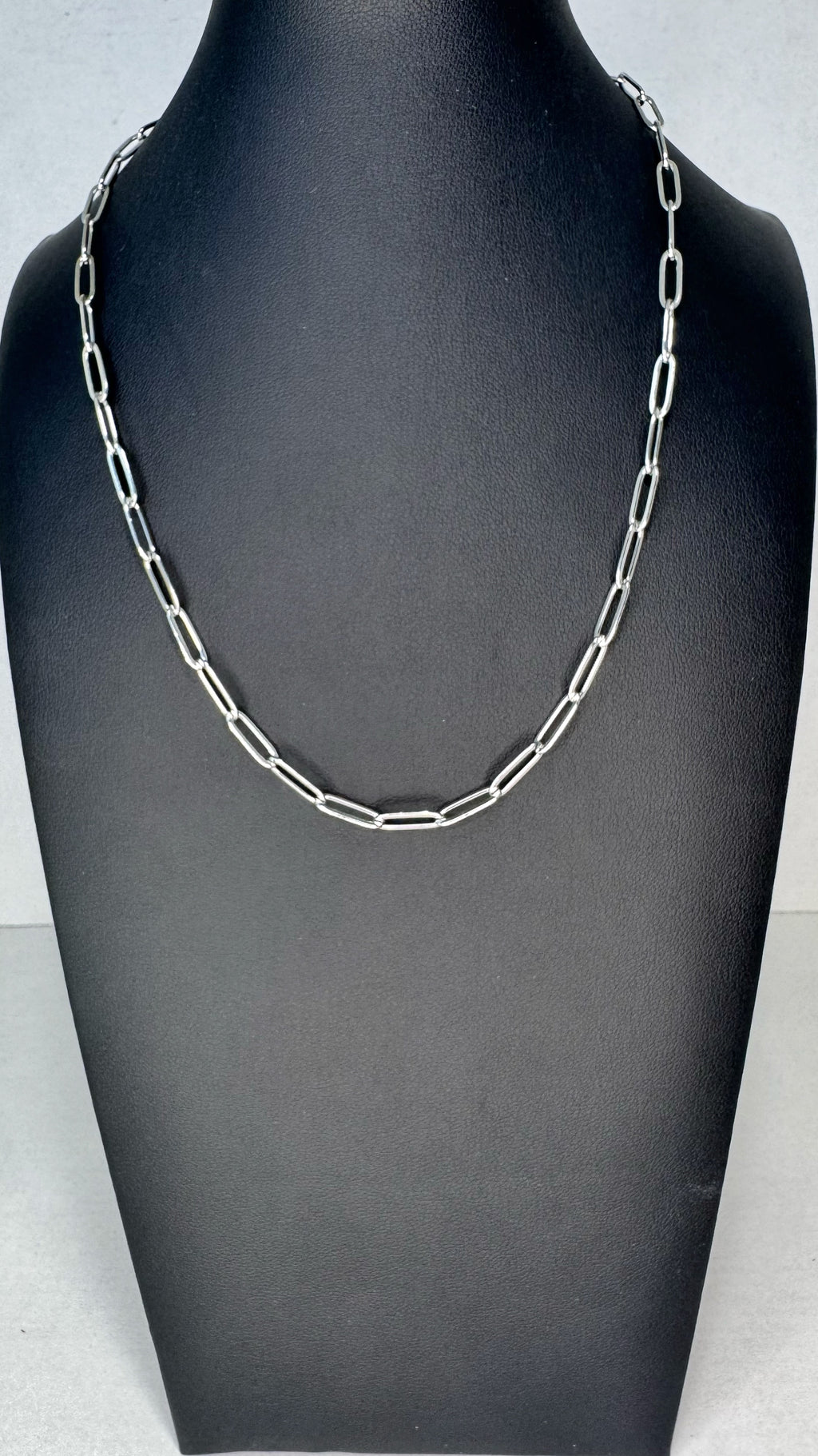 A silver paperclip chain necklace displayed on a black jewelry bust against a light gray background.