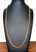A gold-toned Franco chain necklace displayed on a black jewelry bust against a white background with a wooden surface visible at the bottom.