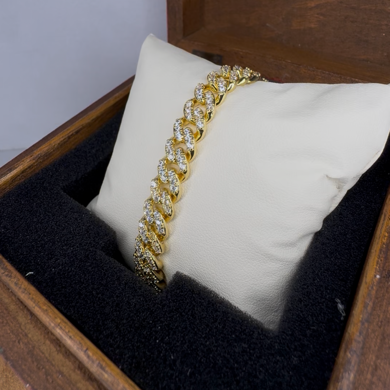Gold bracelet on a white pillow inside a wooden jewelry box with a gray background