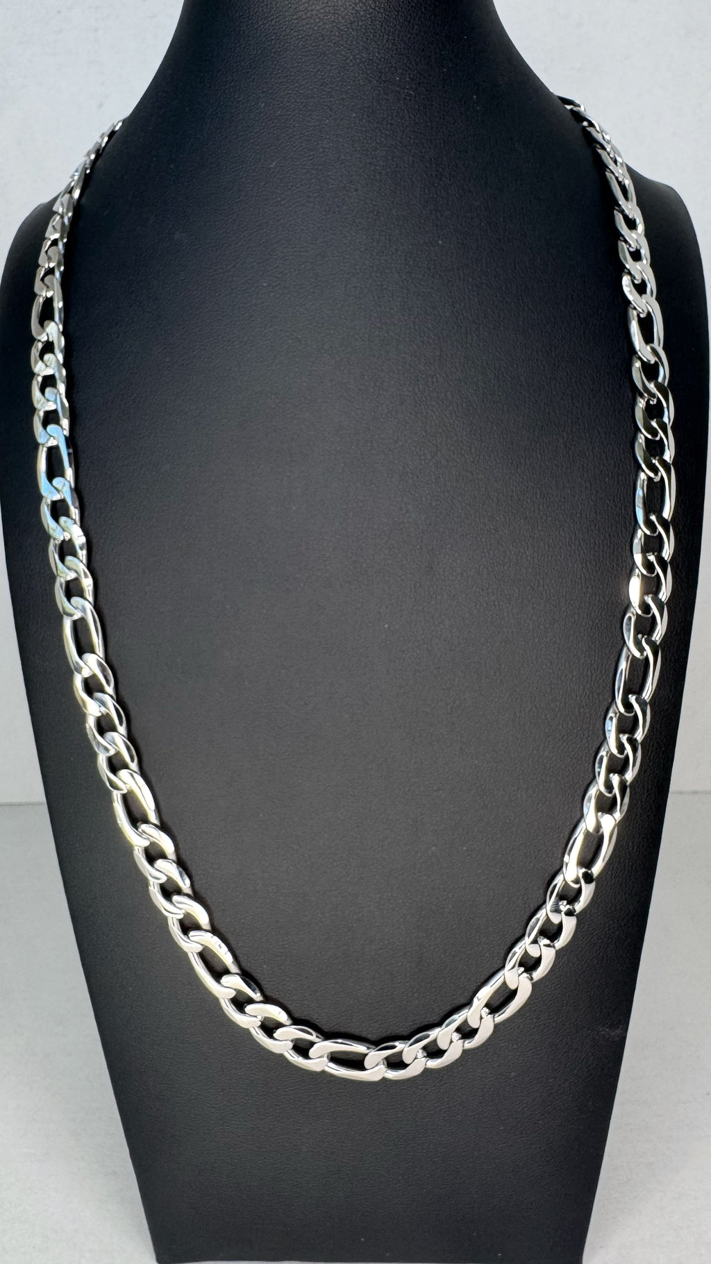 A chunky silver-tone metal Figaro chain necklace displayed on a black mannequin bust against a light gray background.
