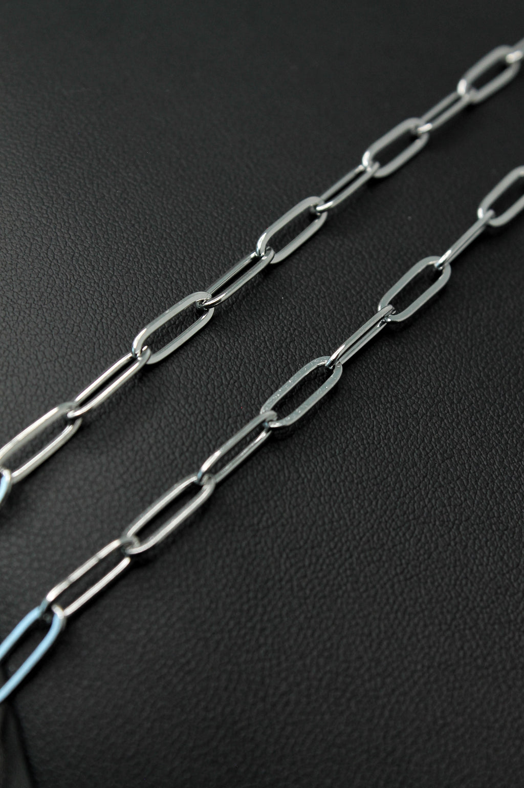 A close-up of a silver paperclip chain laid diagonally across a textured black surface.