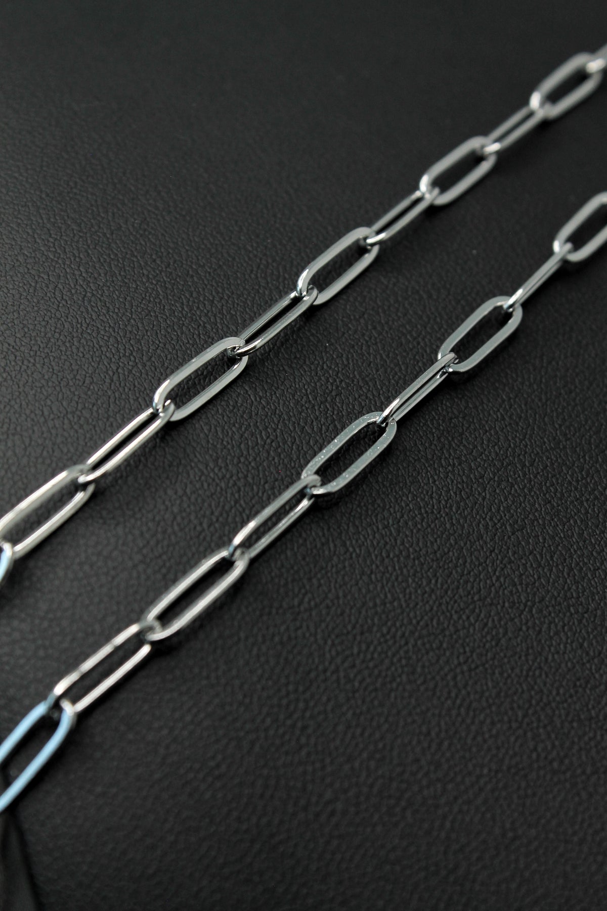 A close-up of a silver paperclip chain laid diagonally across a textured black surface.