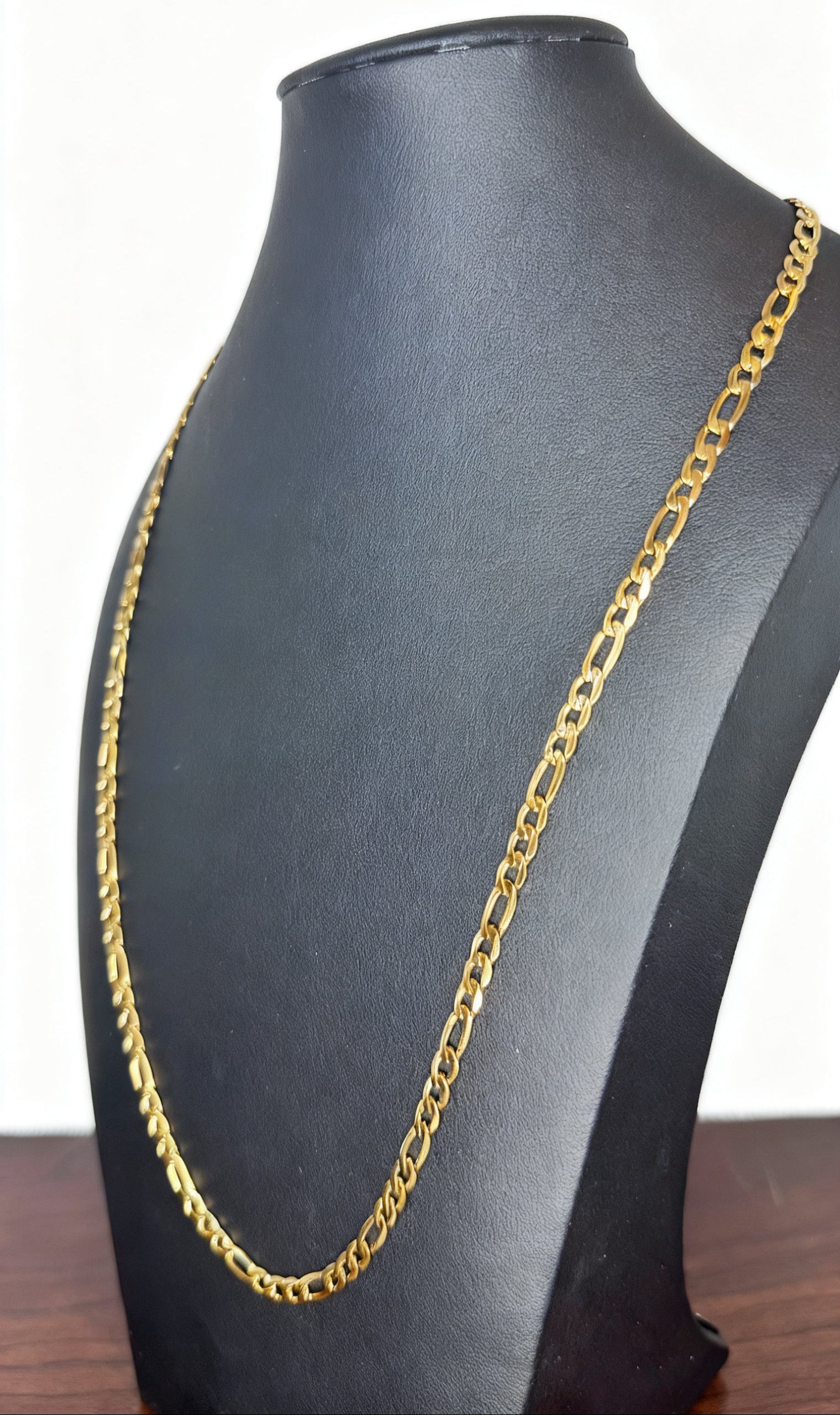 A gold-colored Figaro chain necklace displayed on a black jewelry bust against a white background.