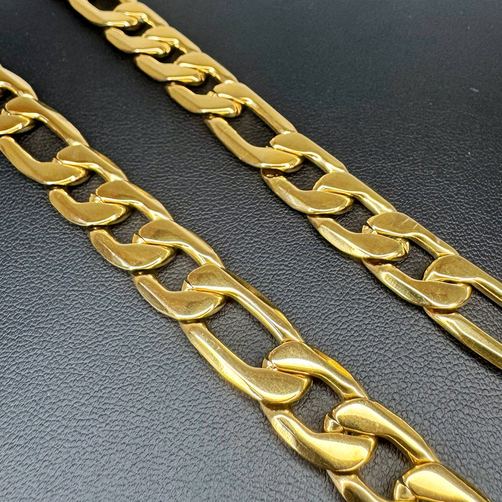 A close-up of a thick gold Figaro link chain laid diagonally across a textured black surface.