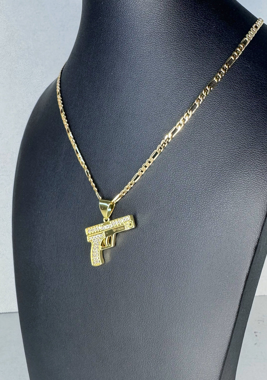Gold necklace with a gun-shaped pendant on a black mannequin bust.