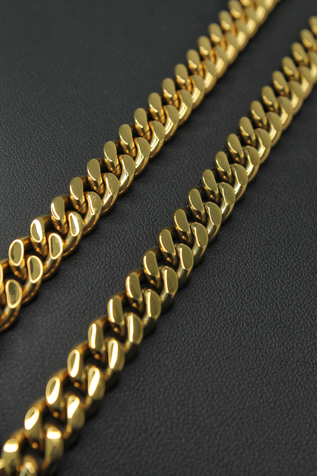 A close-up of a shiny gold Curb link chain laid diagonally across a dark textured surface.