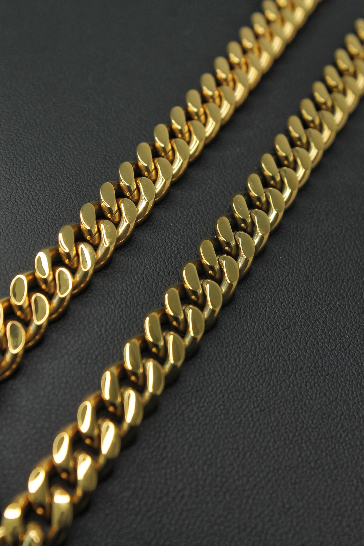 A close-up of a shiny gold Curb link chain laid diagonally across a dark textured surface.