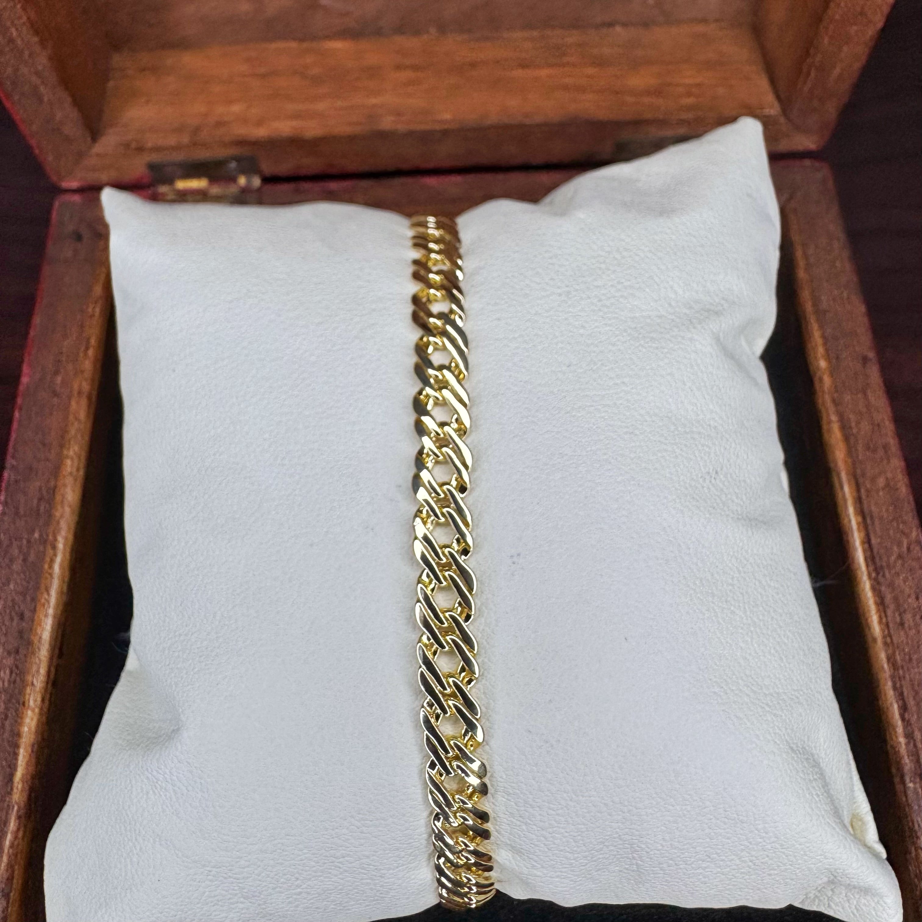 Gold chain bracelet on a white cushion inside a wooden jewelry box