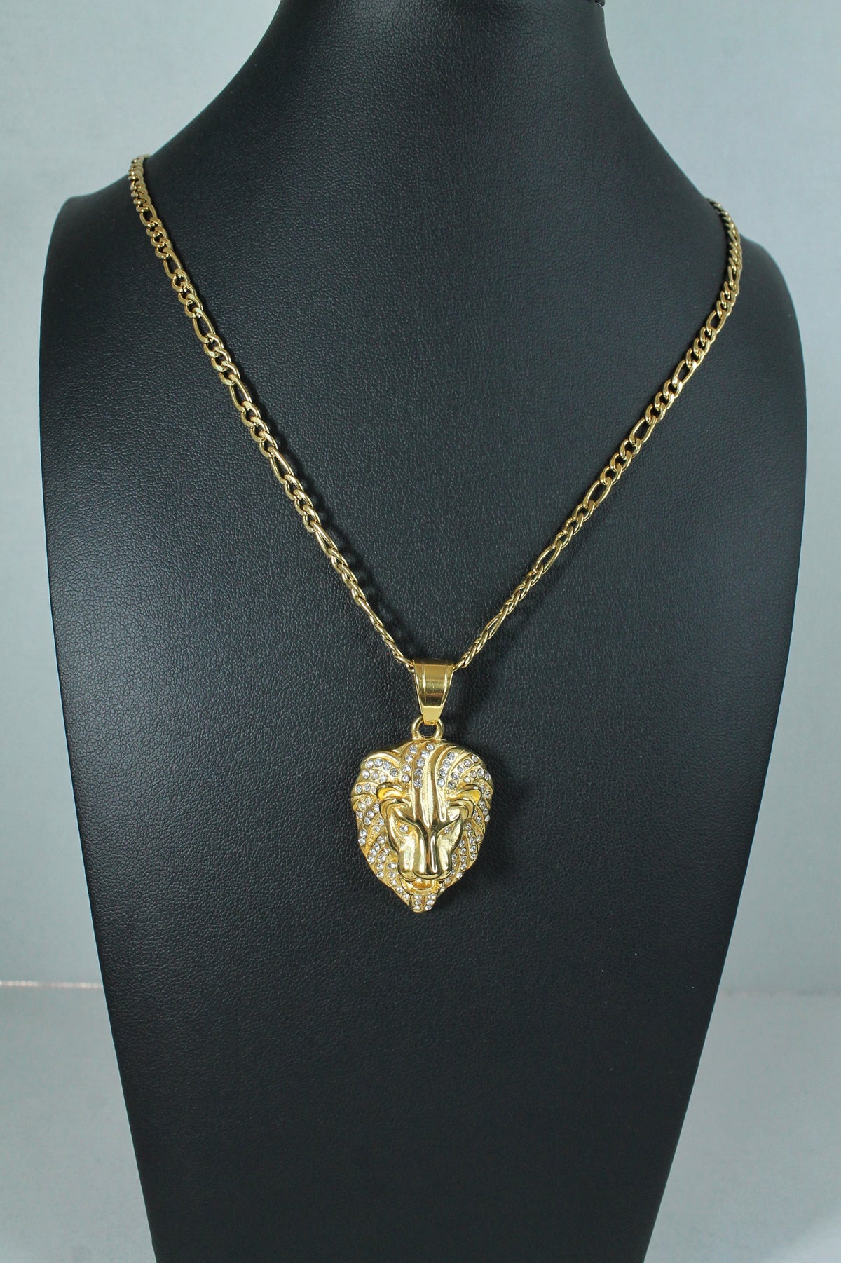 A gold lion head pendant necklace displayed on a black mannequin bust against a light gray background.