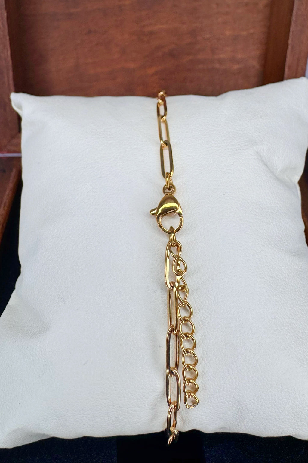 A gold-toned chain link bracelet with a lobster clasp and an adjustable extender chain, displayed on a white pillow.