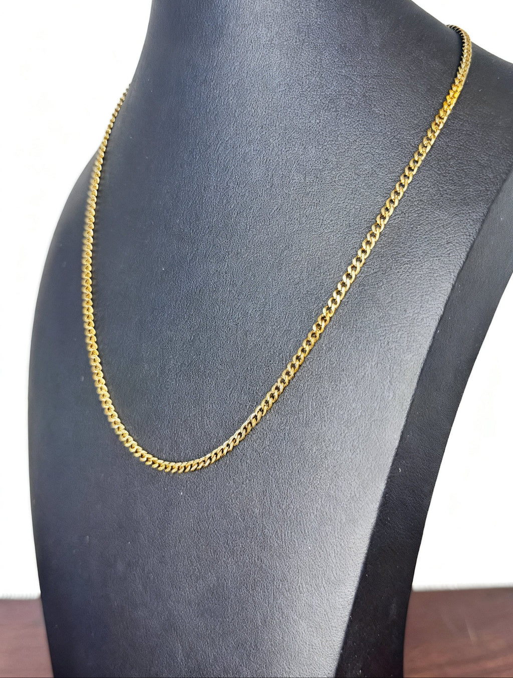 A gold-toned curb chain necklace displayed on a black jewelry bust against a white background.