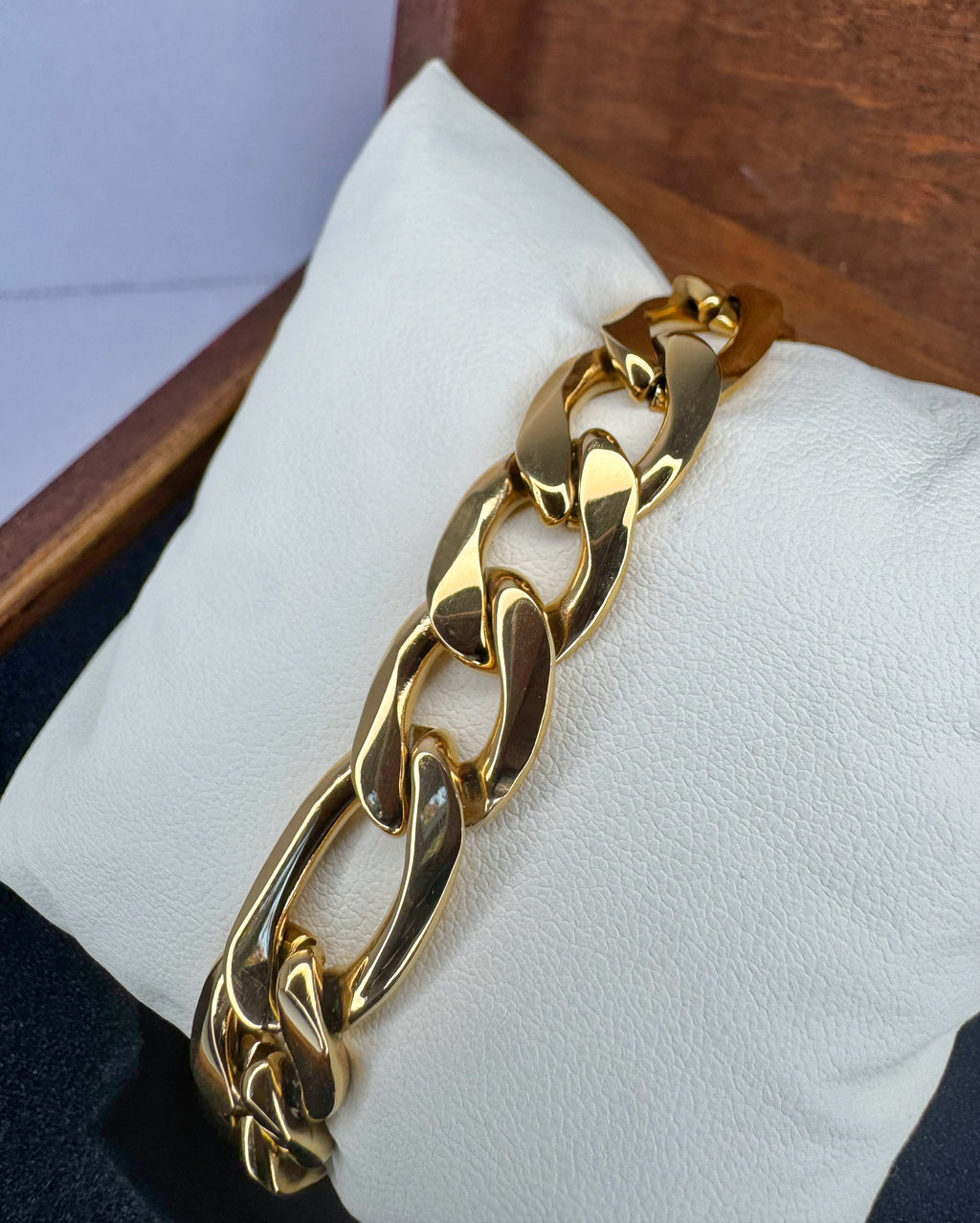 Gold chain bracelet on a white cushion with a wooden background