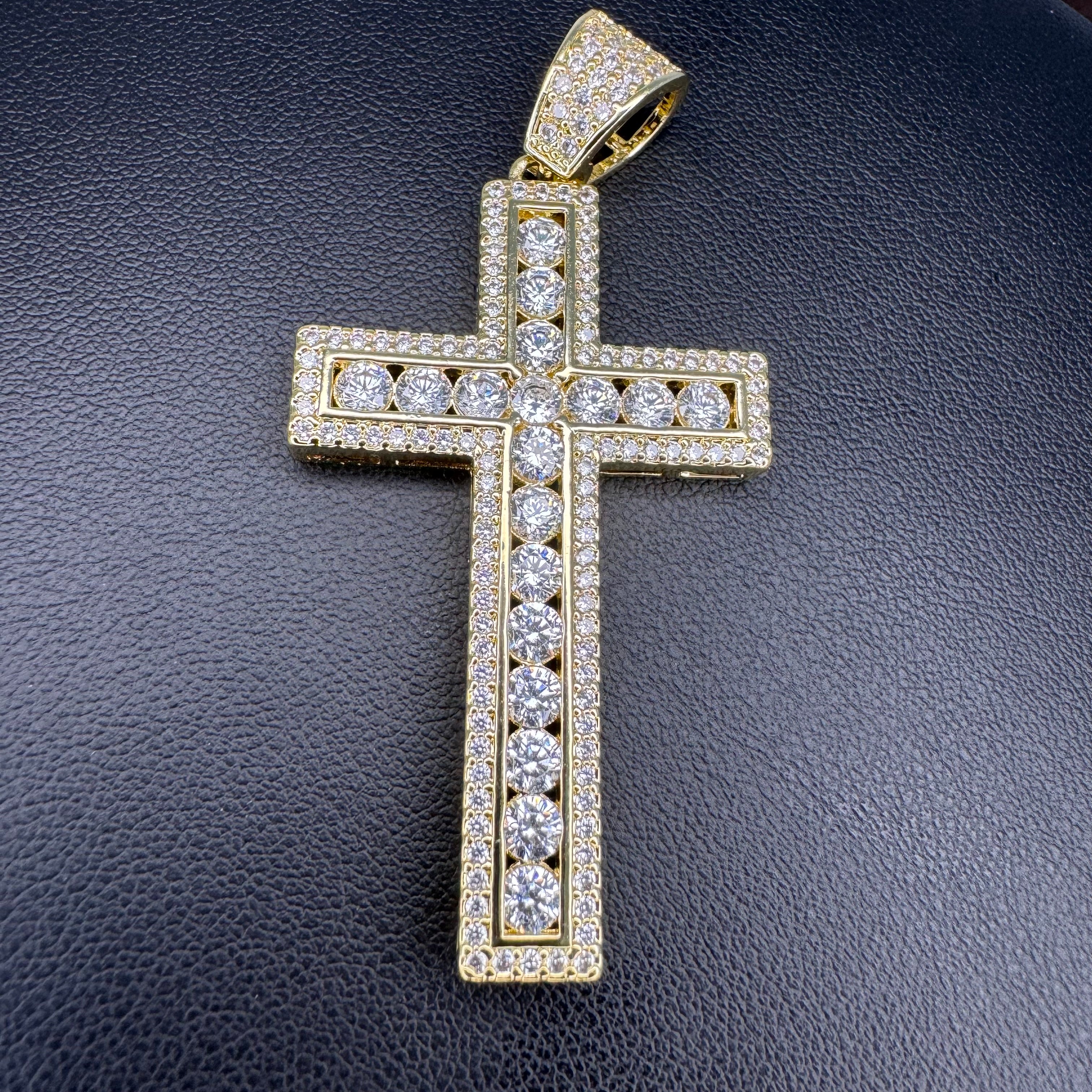 A gold cross pendant encrusted with clear cubic zirconia stones, displayed on a textured black background.