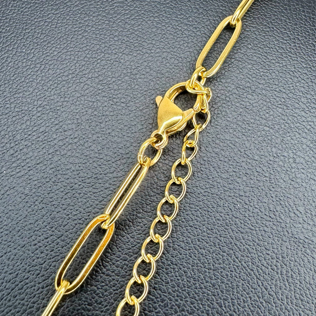 A close-up of a gold-tone chain accessory featuring a paperclip link design, a lobster clasp, and an extension chain, displayed on a textured dark gray surface.