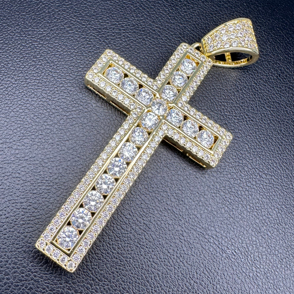 A gold cross pendant encrusted with clear cubic zirconia stones, displayed on a textured black background.