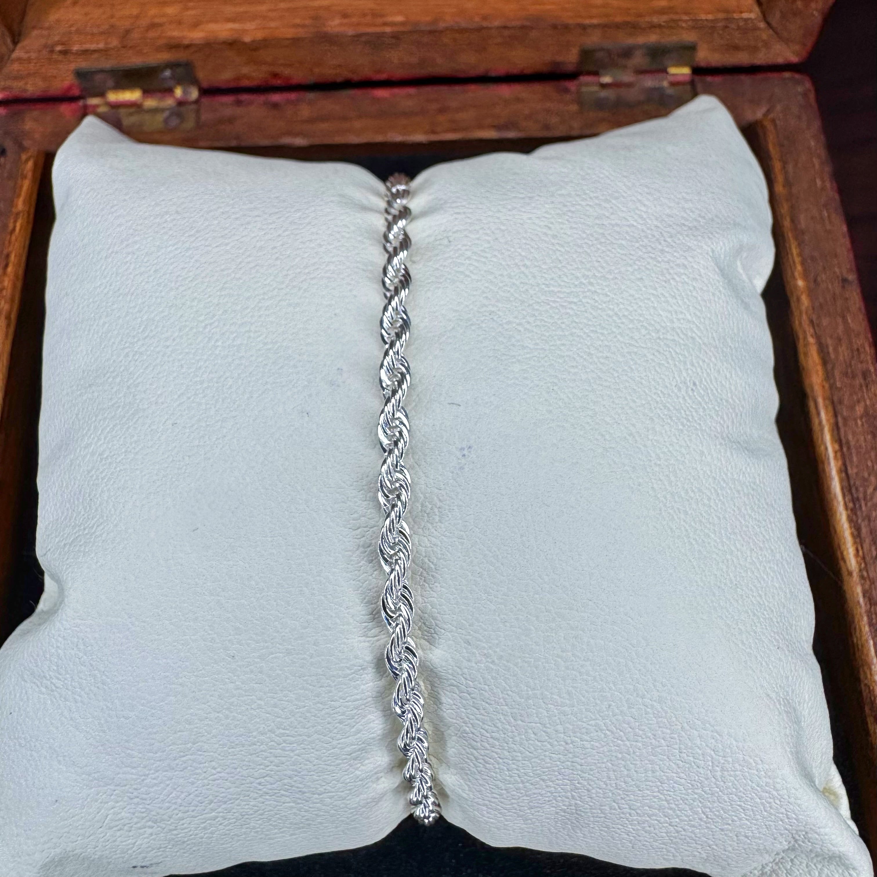 Silver bracelet on a white cushion with a wooden jewelry box in the background
