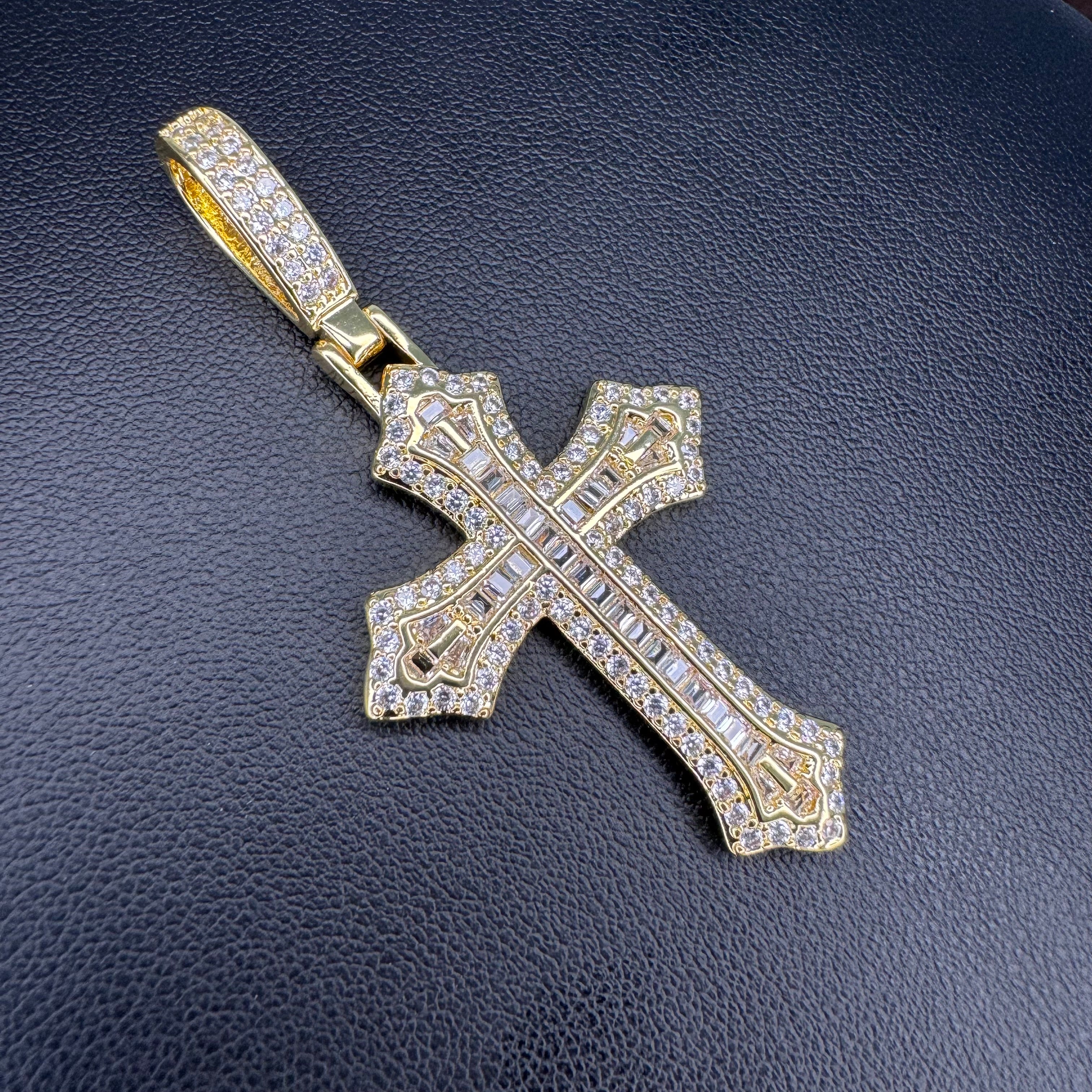 A gold cross pendant encrusted with clear cubic zirconia stones, displayed on a textured black leather background.