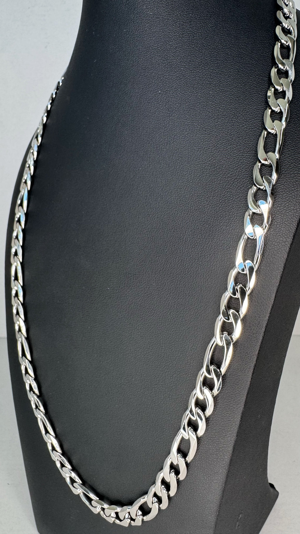 A silver-toned Figaro link chain necklace displayed on a black mannequin bust against a light gray background.