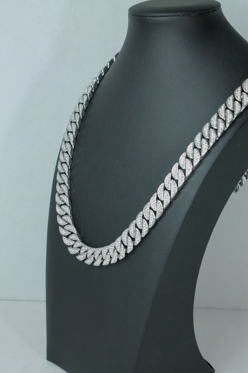 A silver-toned Cuban link chain necklace, heavily embellished with clear rhinestones, displayed on a matte black jewelry bust against a light gray background.