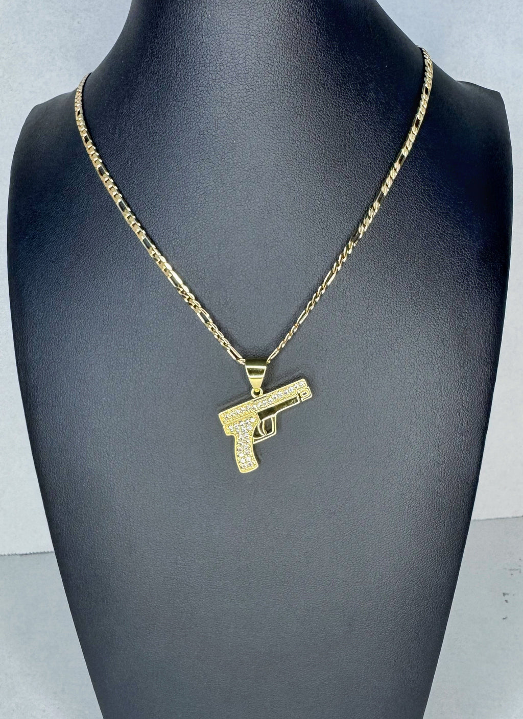 Gold gun-shaped pendant on a chain displayed on a mannequin neck.
