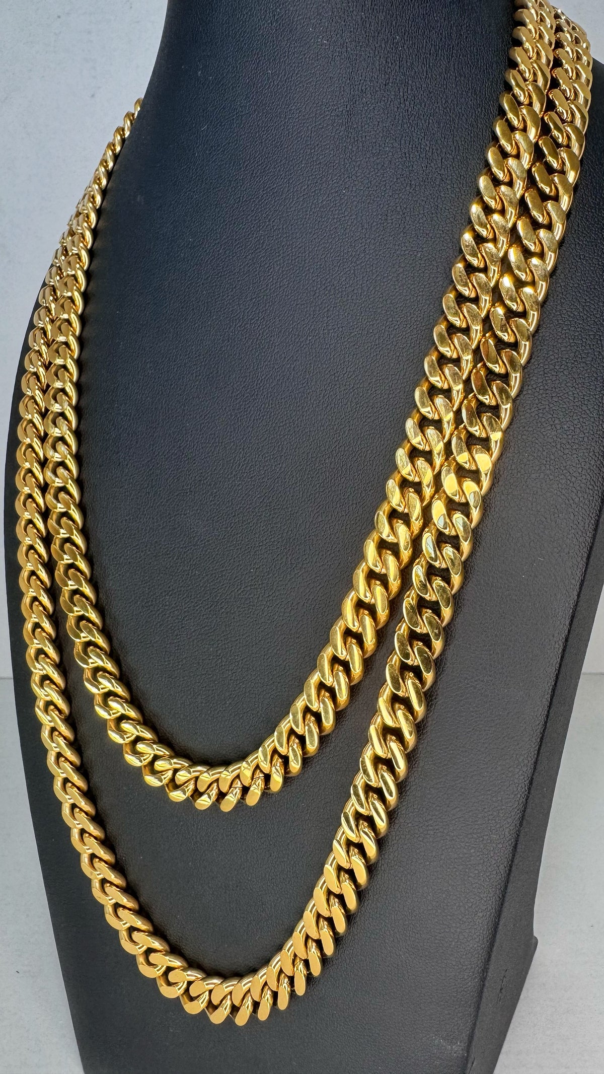 Two thick gold Curb link chains draped over a black display bust against a light gray background.