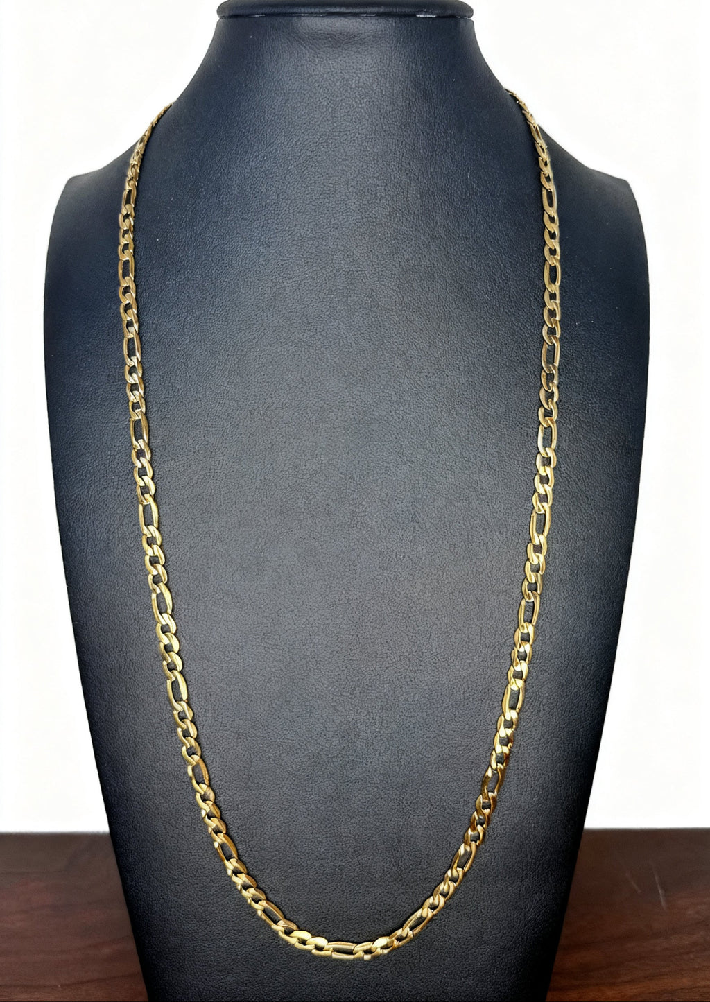 A gold Figaro chain necklace displayed on a black jewelry bust against a white background.