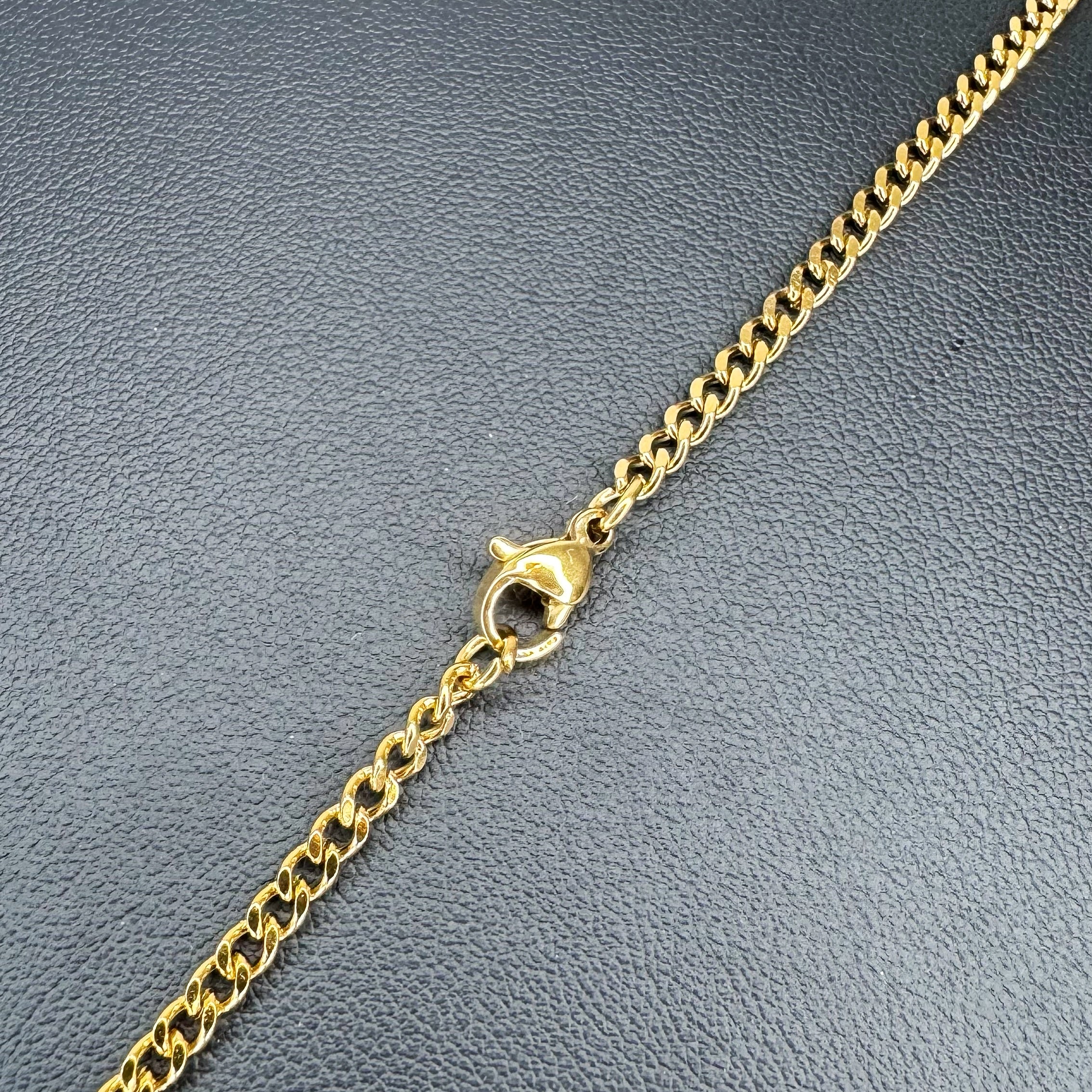 A close-up of a gold-toned metal chain with a lobster clasp, laid diagonally on a textured dark gray surface.