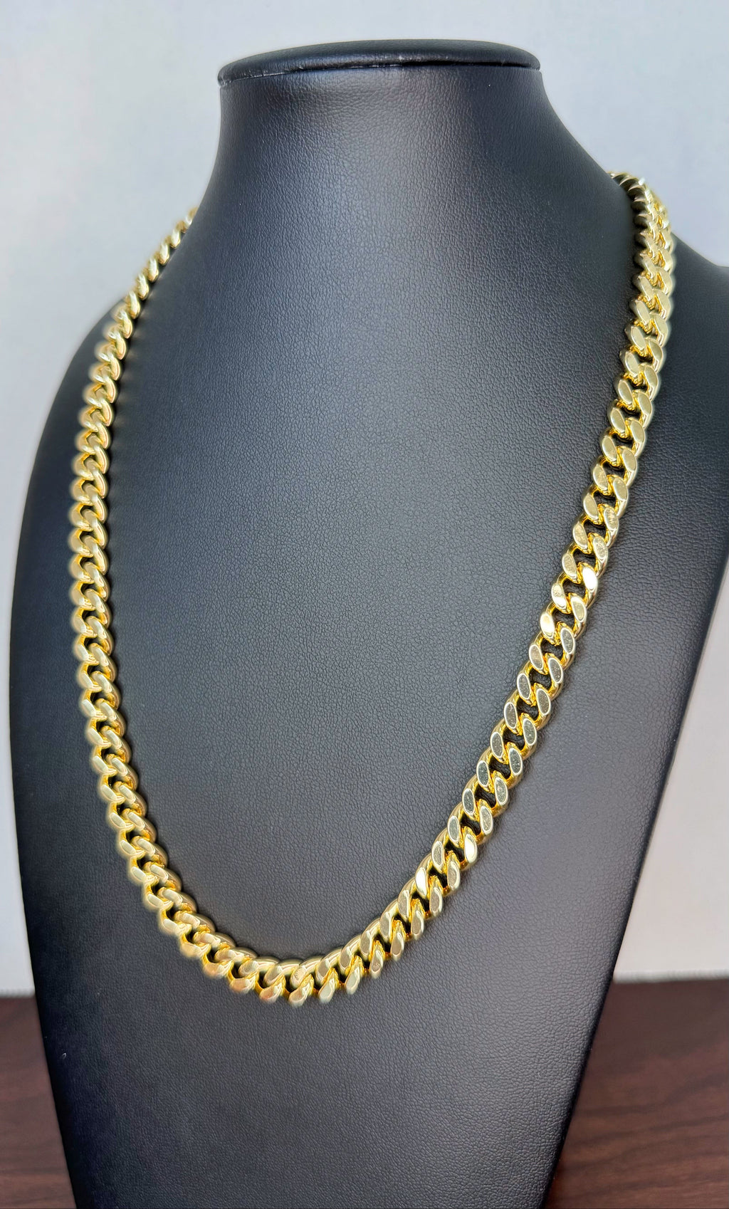 Gold chain necklace on a black mannequin bust against a light gray background