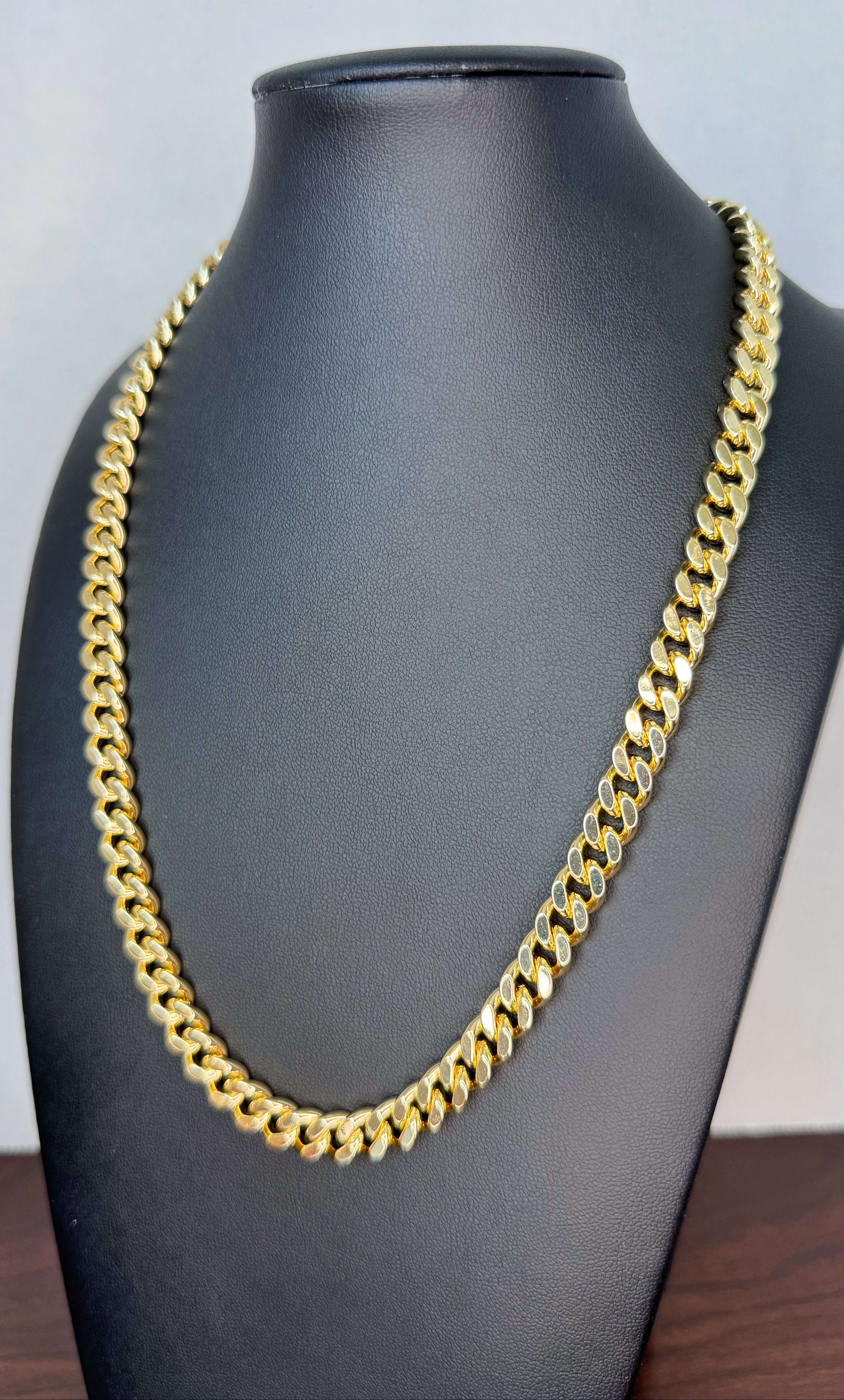Gold chain necklace on a black mannequin bust against a light gray background