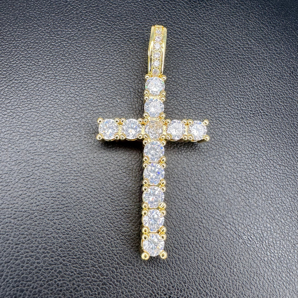 A yellow gold cross pendant adorned with clear cubic zirconia stones, displayed on a textured black surface.