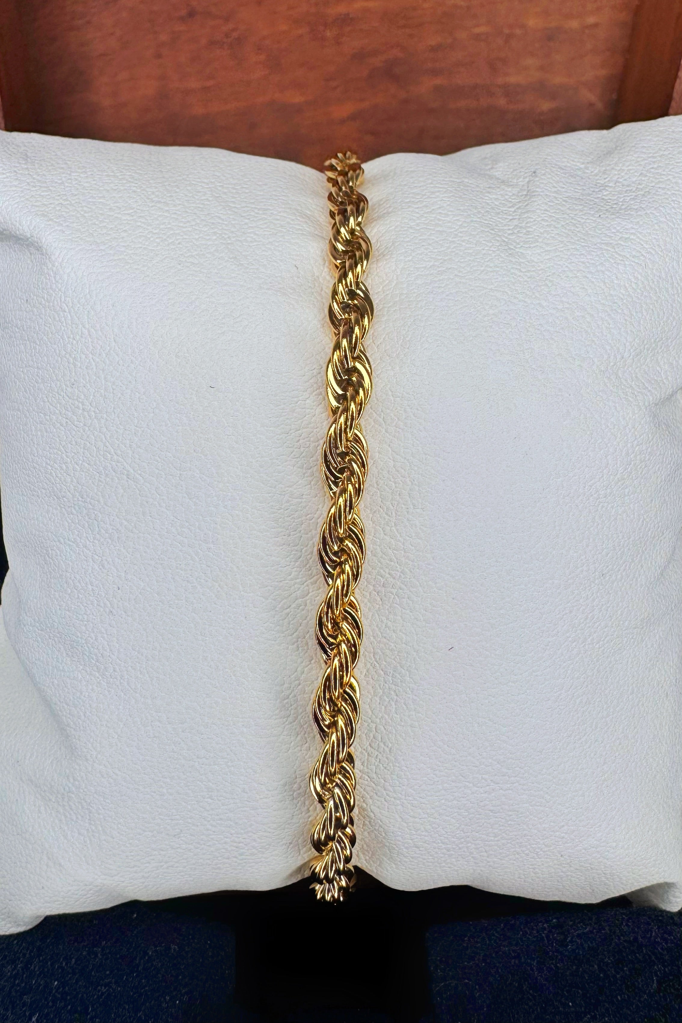 A gold-colored twisted rope chain bracelet displayed vertically on a white textured pillow.