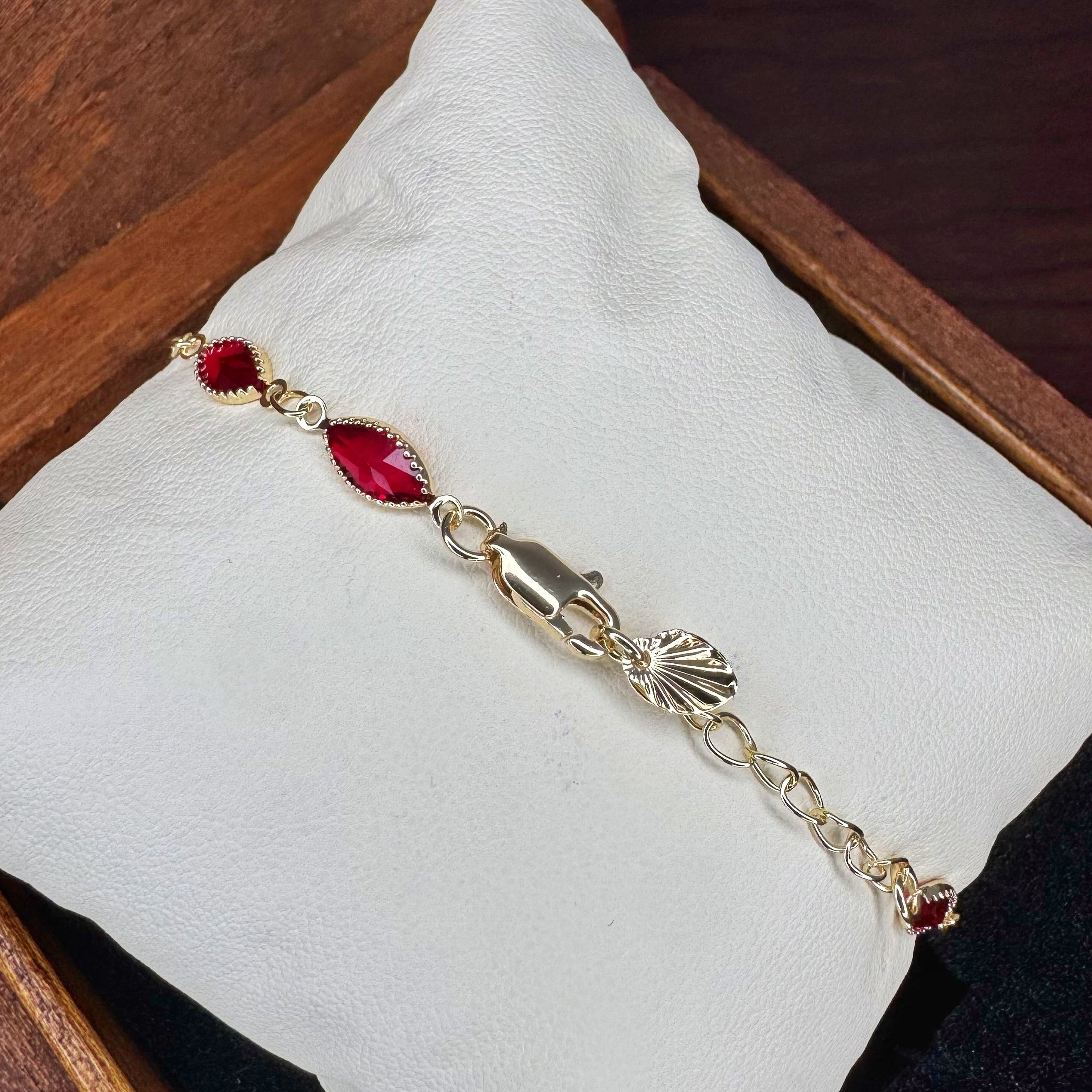 Bracelet with red gemstones and gold chain on a white cushion