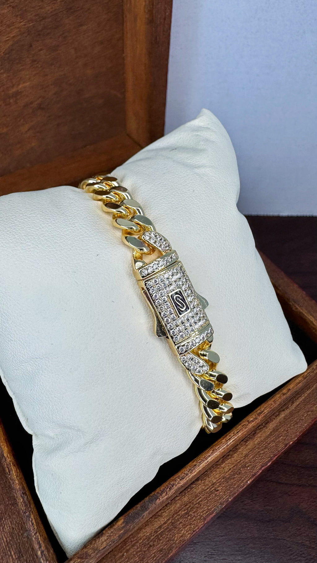 Gold chain bracelet with diamonds on a white pillow inside a wooden box.