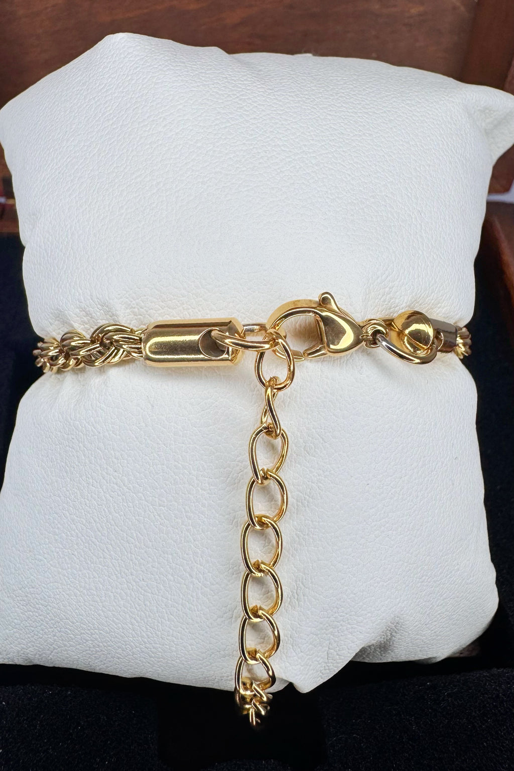 A gold chain bracelet with a lobster clasp and extender chain, displayed on a white cushion.