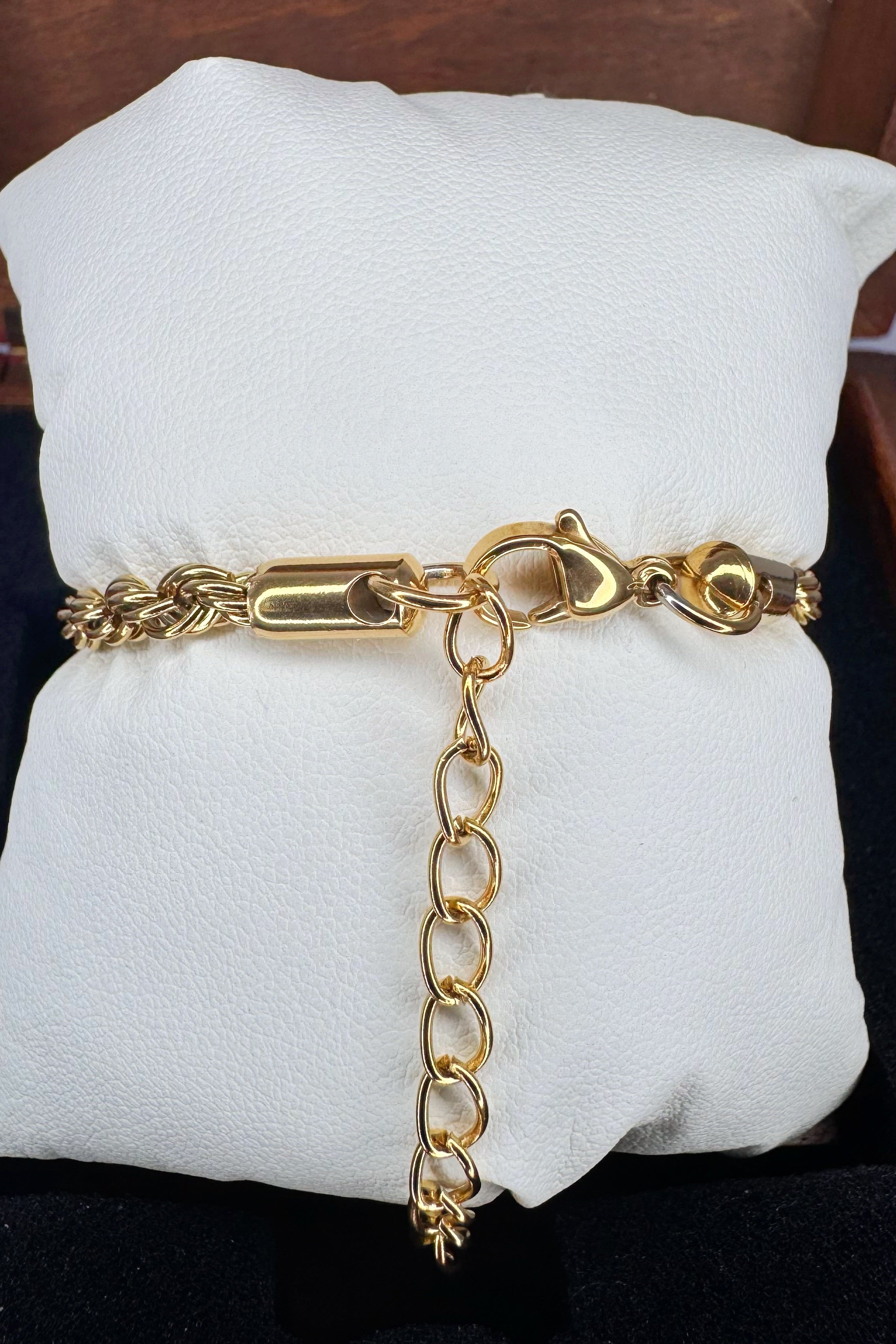 A gold chain bracelet with a lobster clasp and extender chain, displayed on a white cushion.