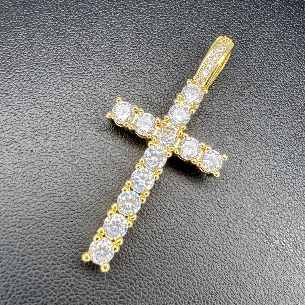 A yellow gold cross pendant encrusted with clear round-cut gemstones, displayed on a textured black surface.