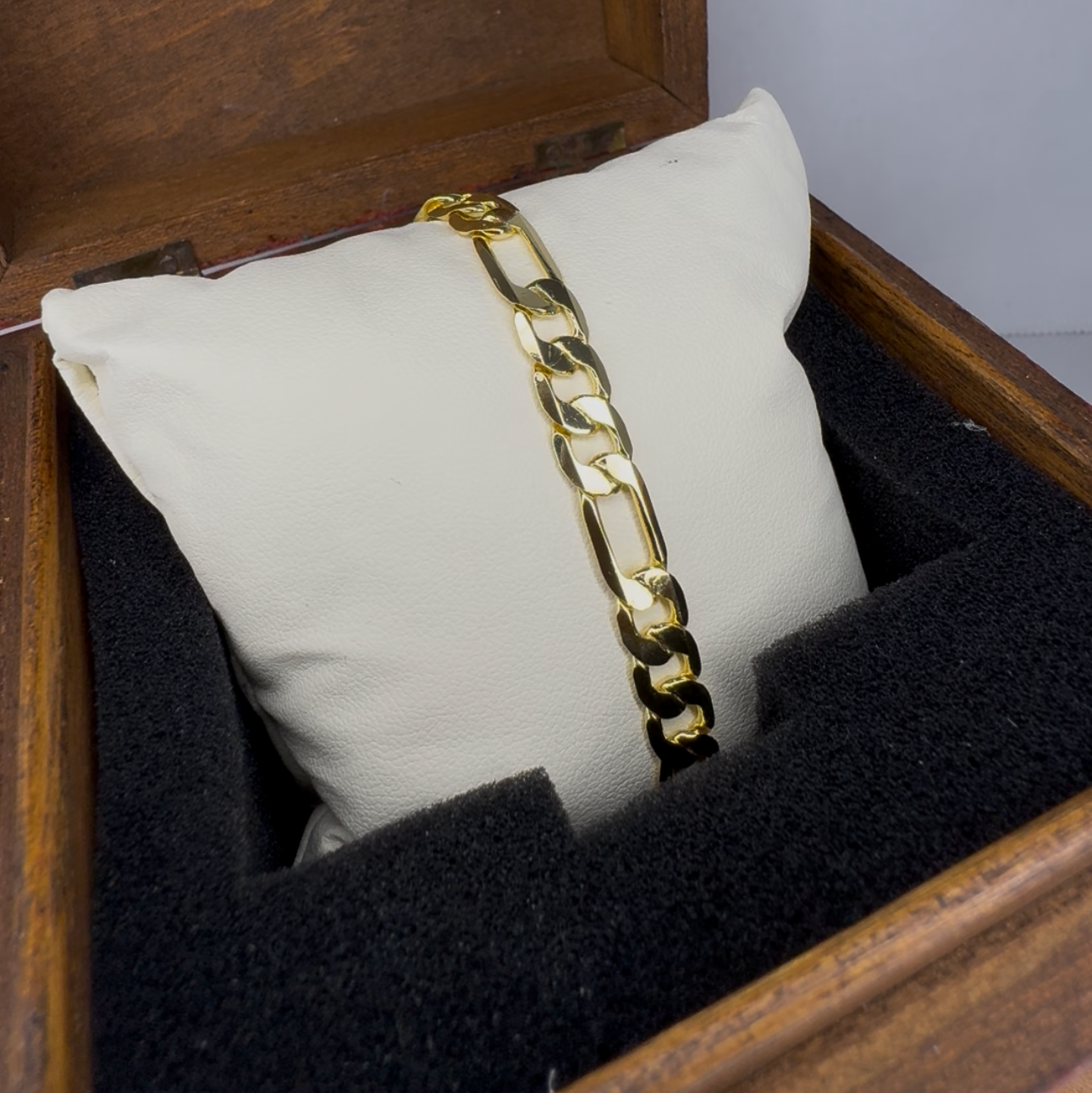 Gold chain bracelet on a white pillow inside an open wooden jewelry box.