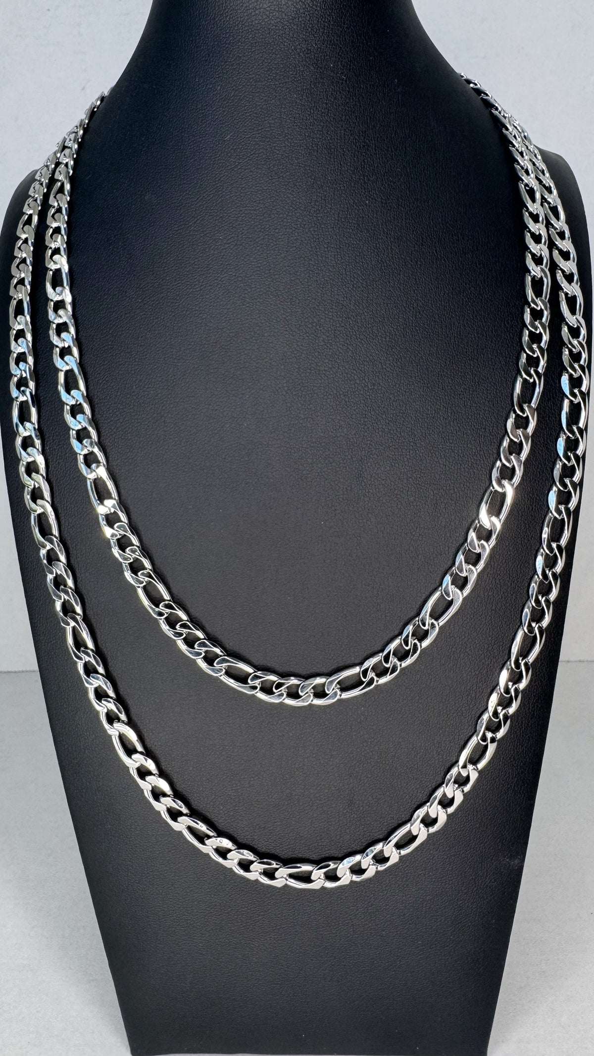 Two layered silver-tone Frigaro chain necklaces displayed on a black mannequin bust against a light gray background.
