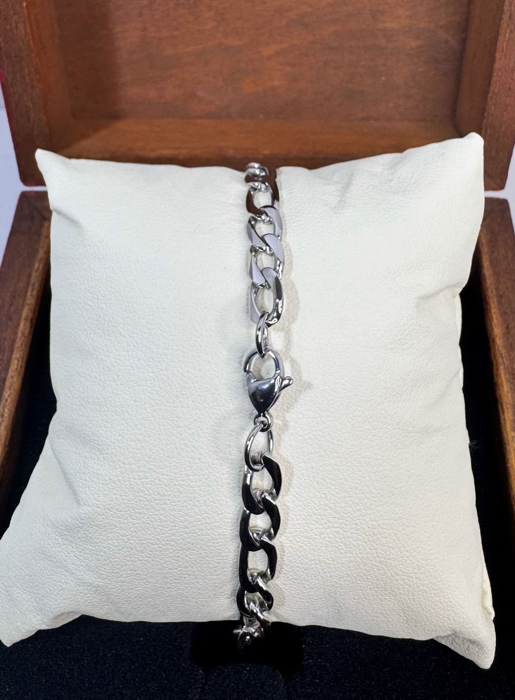 A silver-toned chunky figaro chain bracelet displayed vertically on a white textured pillow inside a wooden box.