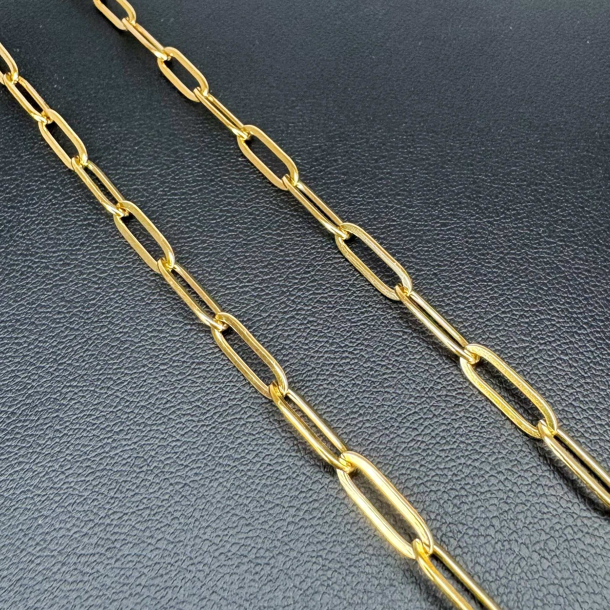A close-up of a gold paperclip chain necklace laid diagonally across a textured black surface.