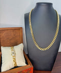 Gold chain necklace displayed on a mannequin bust with a wooden box and pillow in the foreground.