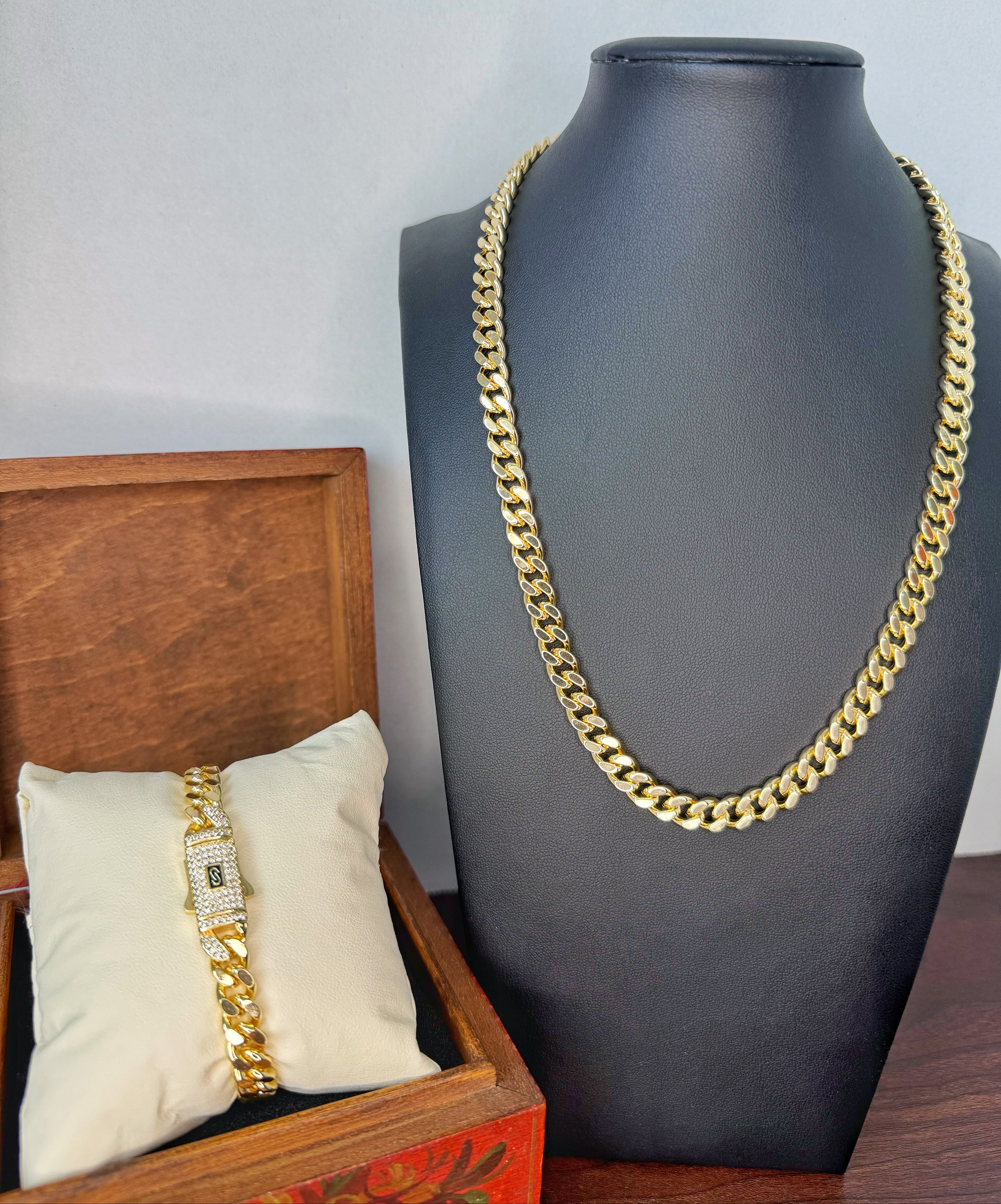 Gold chain necklace displayed on a mannequin bust with a wooden box and pillow in the foreground.