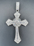 A silver-toned cross pendant encrusted with clear baguette and round-cut stones, displayed on a textured dark gray background.