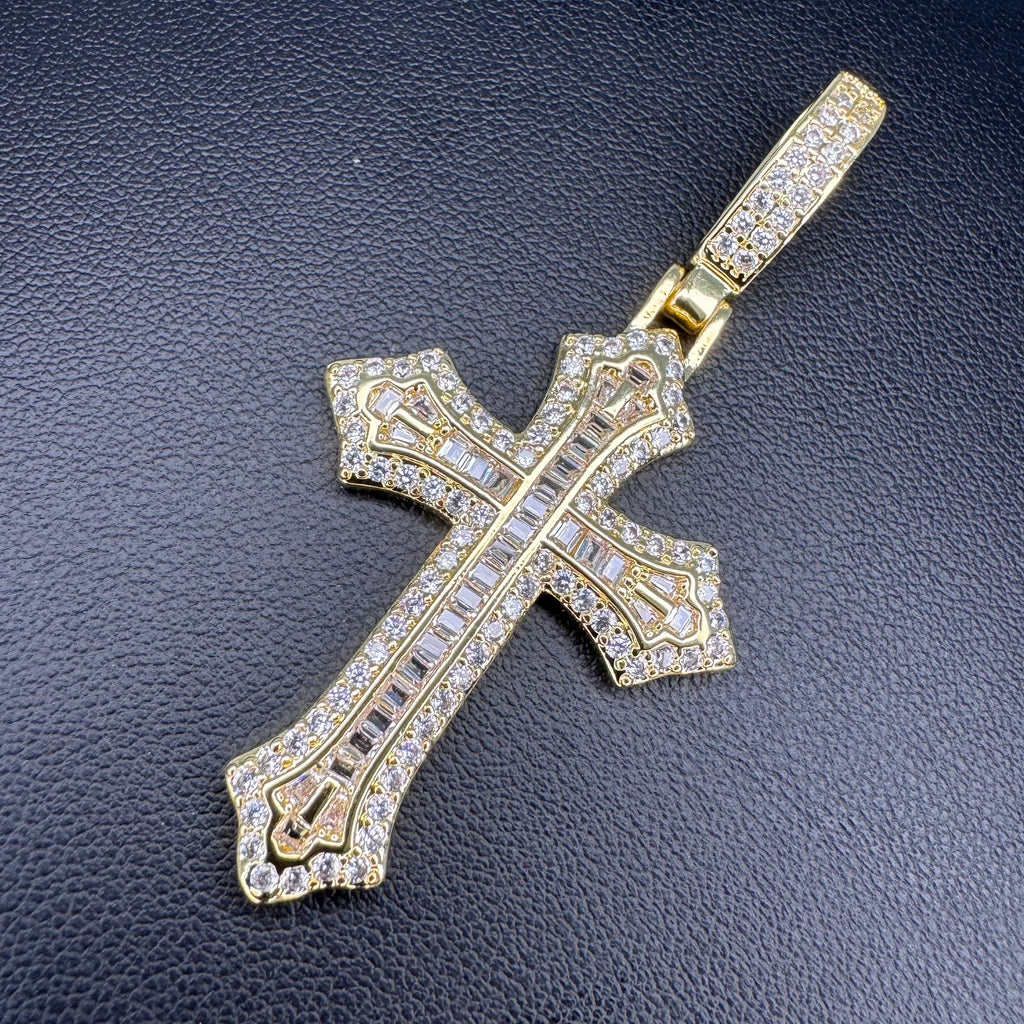 A gold cross pendant encrusted with clear stones, displayed on a textured black surface.