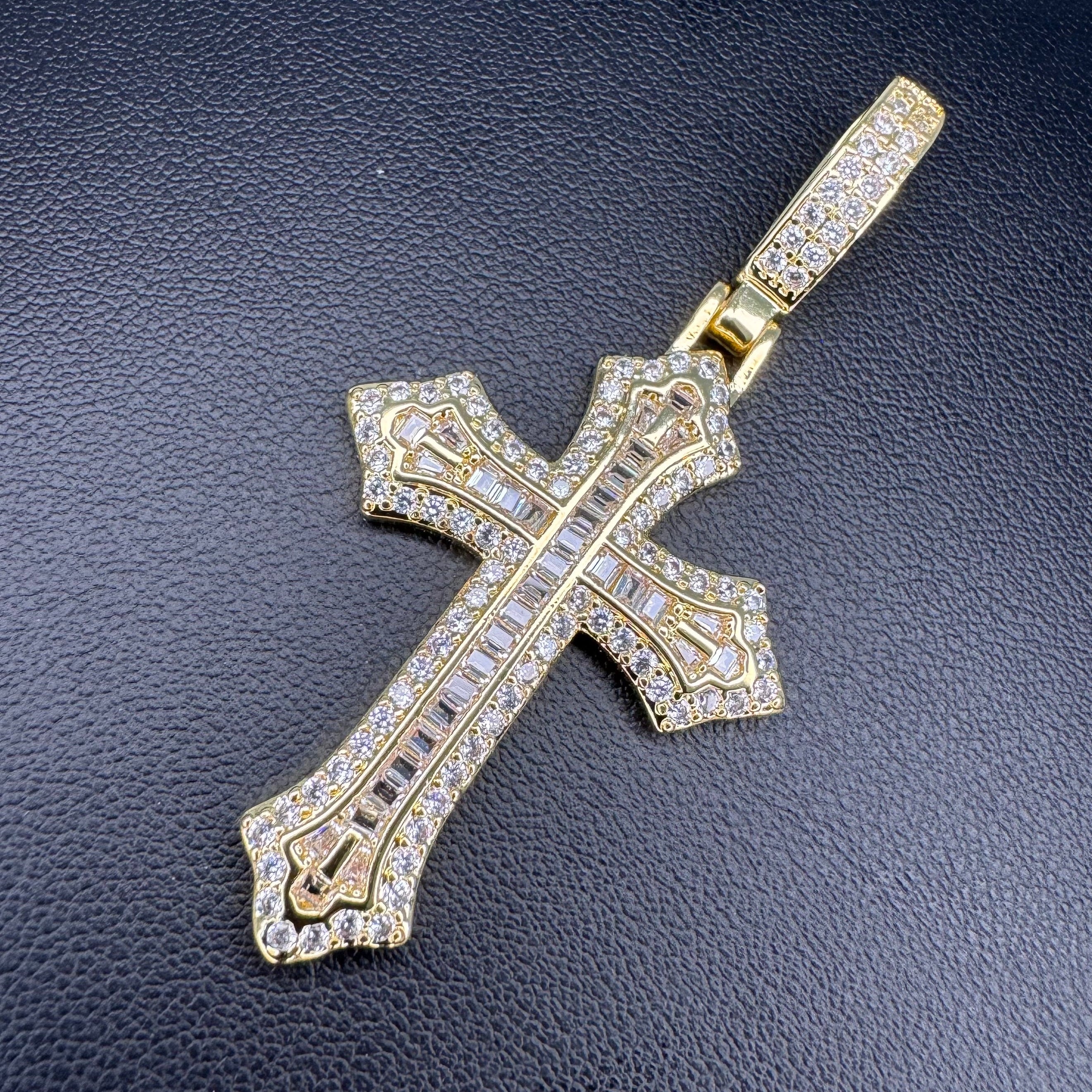 A gold cross pendant encrusted with clear stones, displayed on a textured black surface.