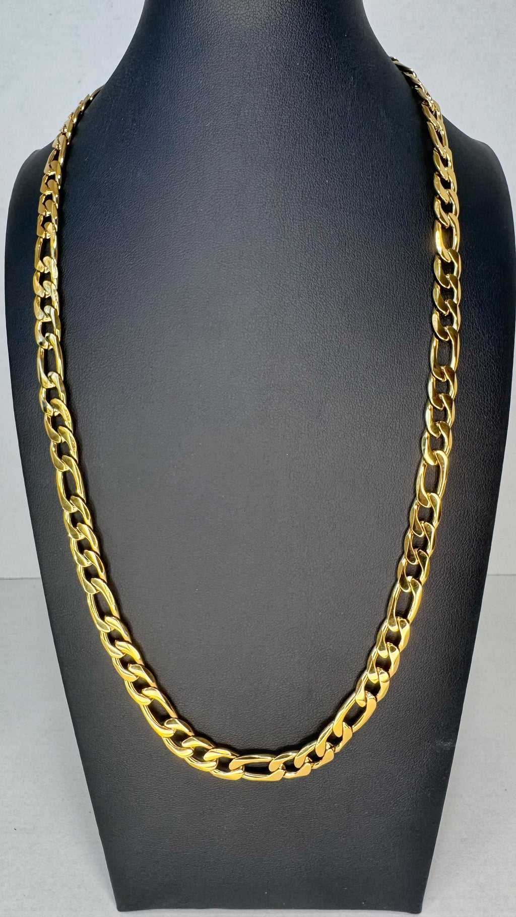 A chunky gold Figaro link chain necklace displayed on a black mannequin bust against a light gray background.
