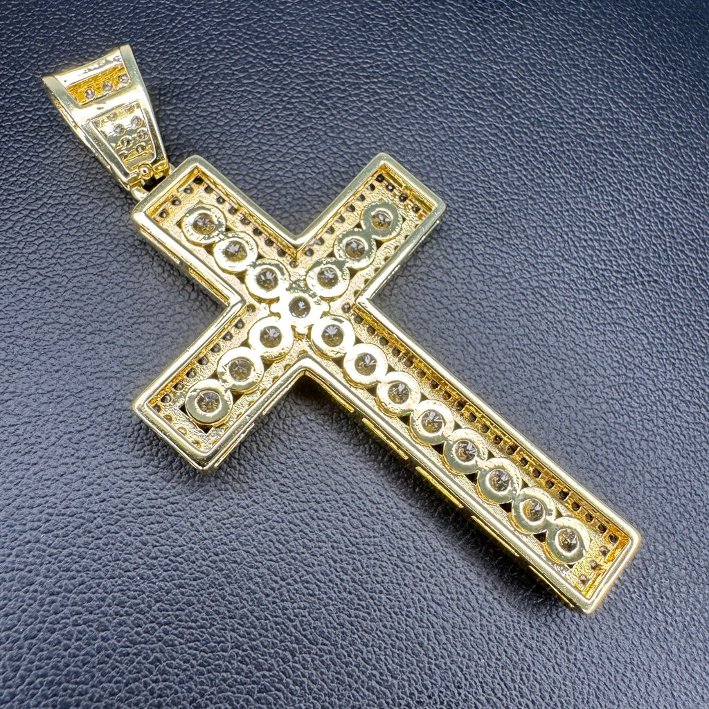 A gold cross pendant with intricate circular detailing and a bail, displayed on a textured dark gray surface.