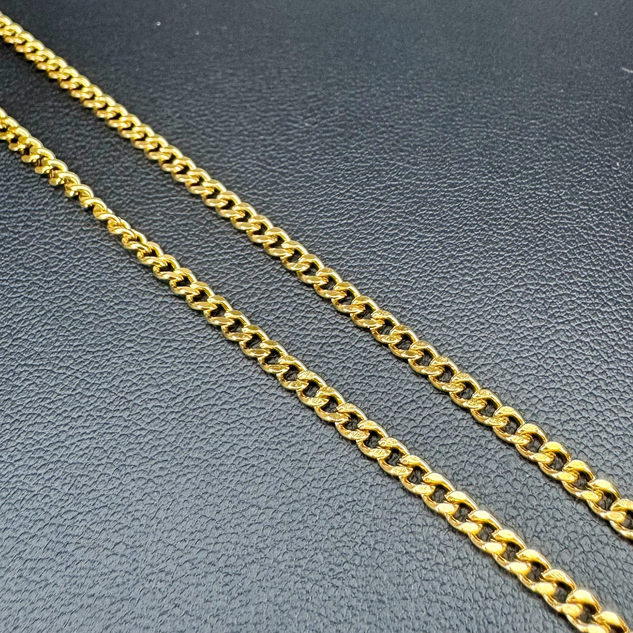 A close-up of a shiny gold Cuban link chain laid diagonally across a textured dark gray surface.