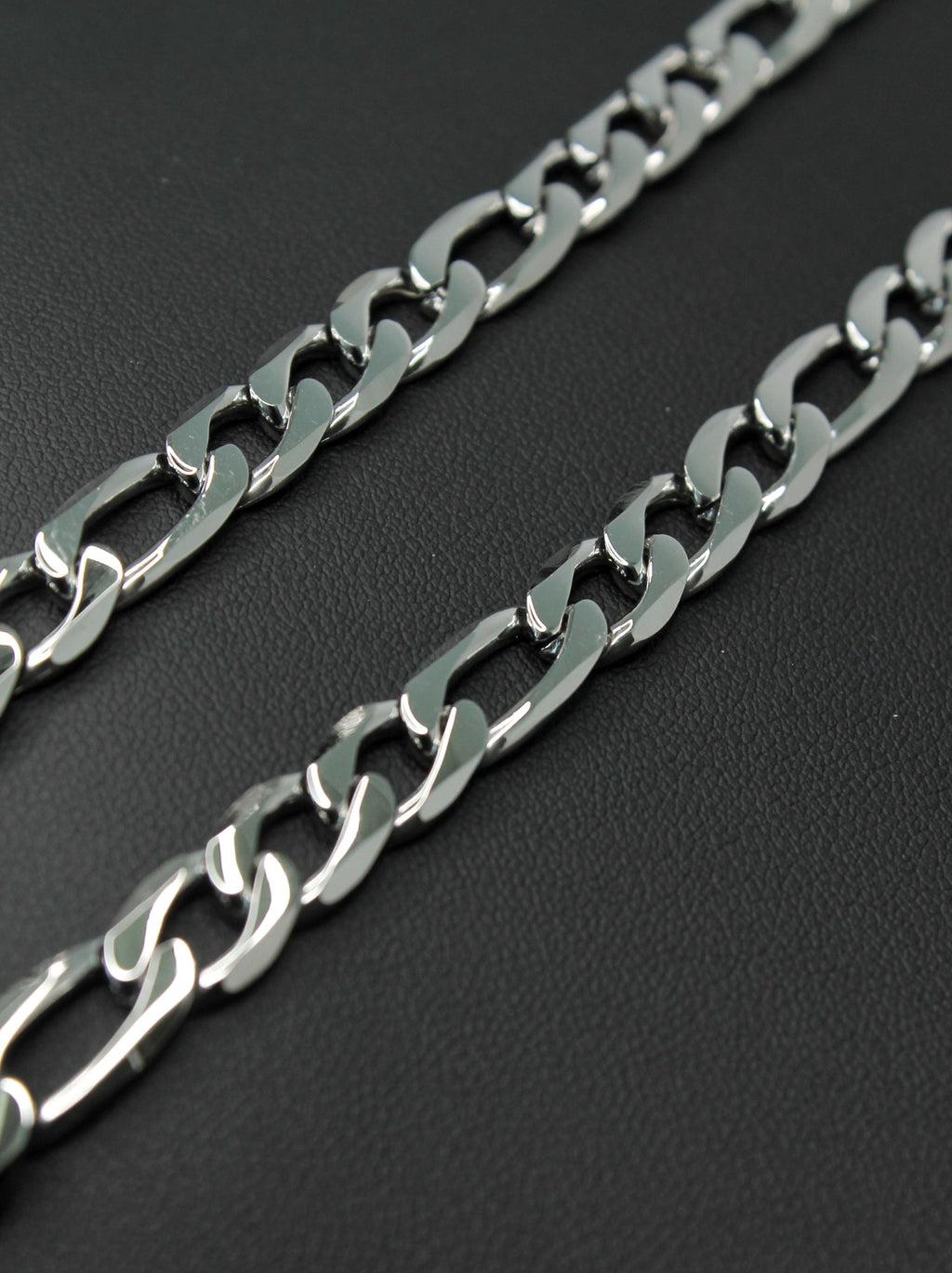 A close-up of a polished silver-tone metal Figaro chain with large interlocking links, laid diagonally on a dark textured background.