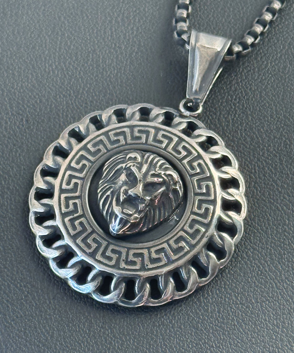 Silver lion head pendant on a chain against a gray background